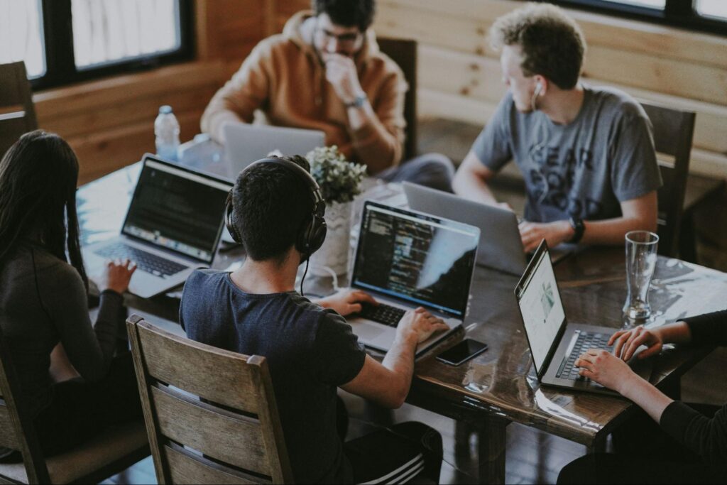People working on laptops around a shared table in a casual office setting.
