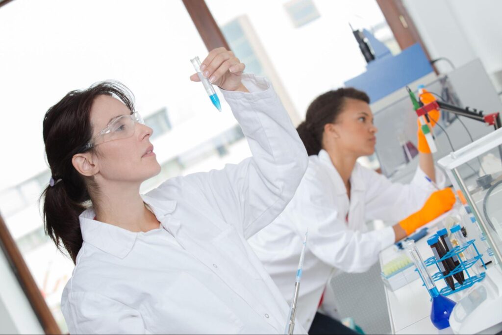 Two scientists in lab coats working with test tubes and lab equipment.